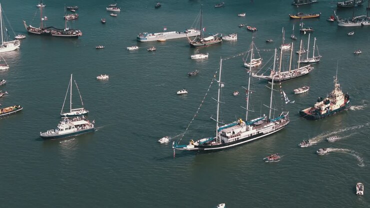 Aerial drone retreats over sailboats during lively Amsterdam Sail event, establishing cultural event
