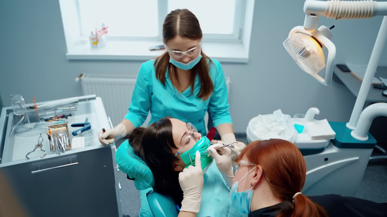 Professional woman dentist at work in clinic. Stomatologist and assistant treating teeth to woman patient on dental equipment background. Top view.