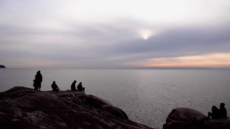 silhouetted people hang out to watch sunset on coastline, long shot