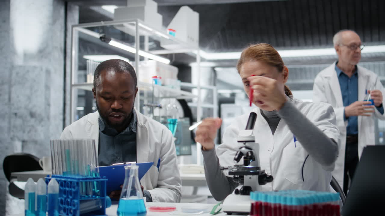 Pathologist examining biopsy slide while colleague documents diagnostic findings