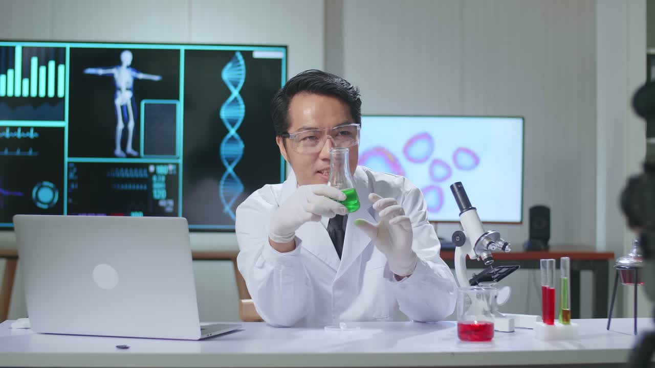Young Asian Male Research Scientist Holding Glass Test Tube And Speaking To The Camera