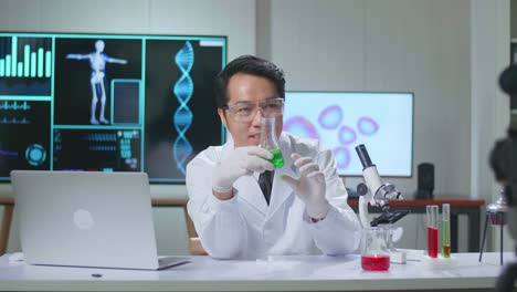 young asian male research scientist holding glass test tube and speaking to the camera
