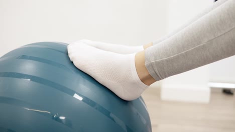 young woman performing lying hip raise exercise with core stability using a physio exercise swiss ball in a sports physiotherapy clinic, close up