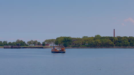 orange roll-on, roll-off ferry leaving the prison dock at hart island, with white prison bus