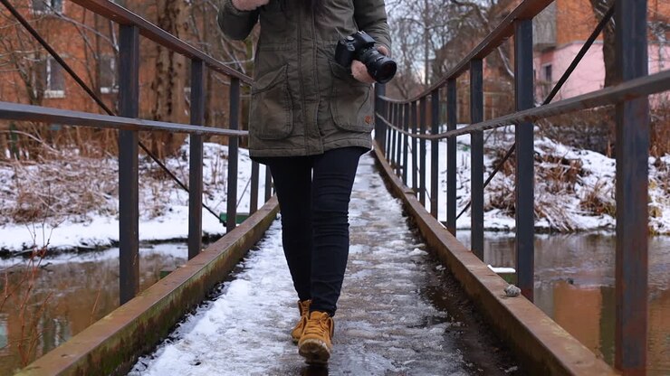Woman walking through snowed bridgeholding a camera.