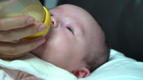 newborn infant baby girl sucking formula milk from the toddler bottle close up on face and mom's hand