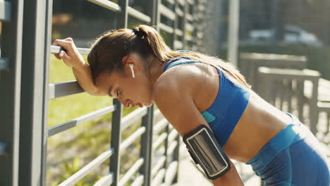 Side-View-Of-A-Tired-Sportswoman-With-Airpods-Resting-And-Breathing-Hard-After-Workout-At-Outdoor-Court-On-A-Summer-Day-1