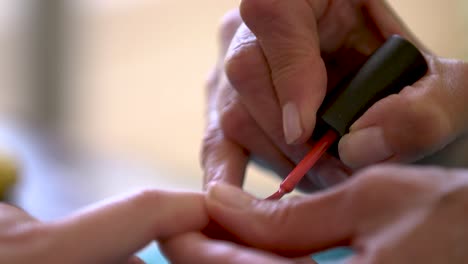 a woman carefully painting a person's nails red