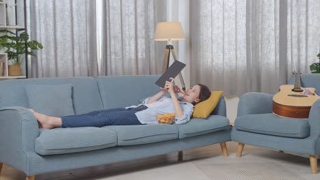 teenager relaxing on couch with tablet and snacks