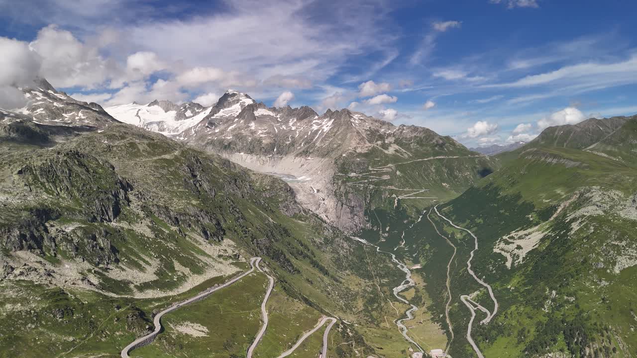 Aerial view of a scenic mountain range near Lake Totensee in Obergoms, Switzerland, featuring a serpentine road winding through the rugged terrain, showcasing the beauty of alpine landscapes.