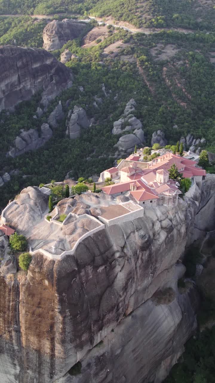 Vertical aerial view showcasing the Monastery of the Holy Trinity perched on a cliff in Meteora, Greece, highlighting its stunning church architecture