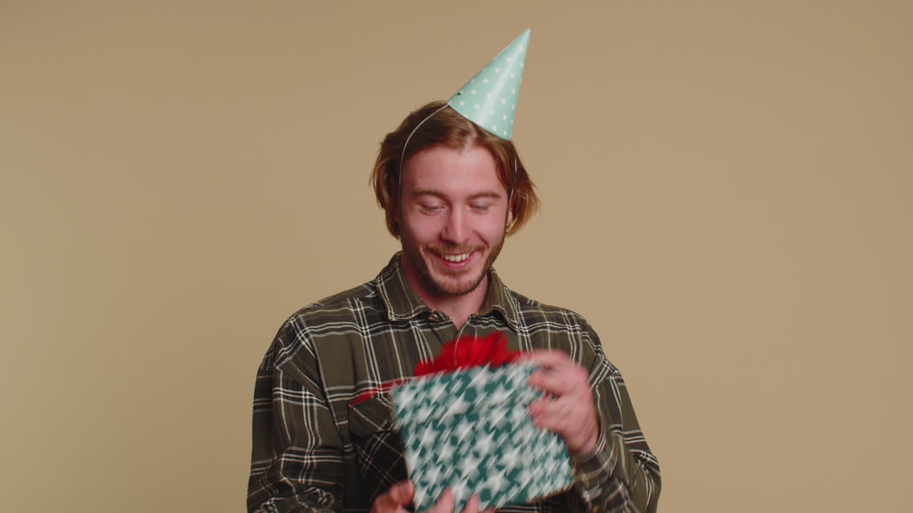 행복한 젊은이가 선물 상자를 열고, 생일 깜짝 선물을 풀고 최고의 선물 보너스에 만족합니다.