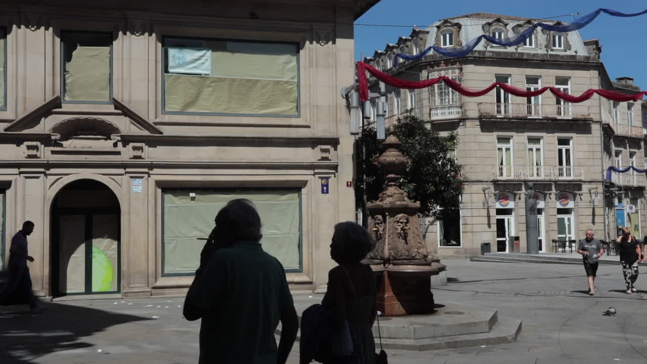 People walking in a historic square with a fountain and decorative banners in Pontevedra, Spain