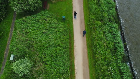 Reeuwijkse-Plassen,-Reeuwijk,-Zuid-holland,-Die-Niederlande---Zwei-Freunde,-Die-Zusammen-Trainieren,-Indem-Sie-Neben-Einem-See-Spazieren-Gehen,-Der-Von-Einer-üppigen-Grünen-Landschaft-Umgeben-Ist