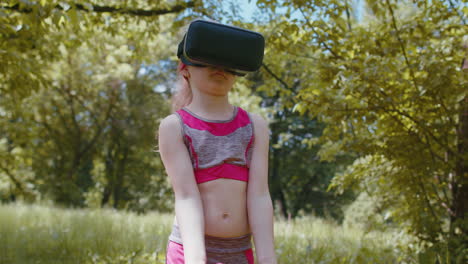niño atlético en casco de auriculares vr haciendo ejercicios de entrenamiento de fitness con pesas al aire libre en el parque