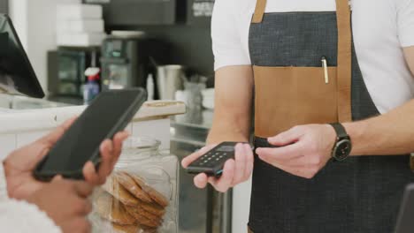 diverse male barista and female customer paying with smartphone in cafe