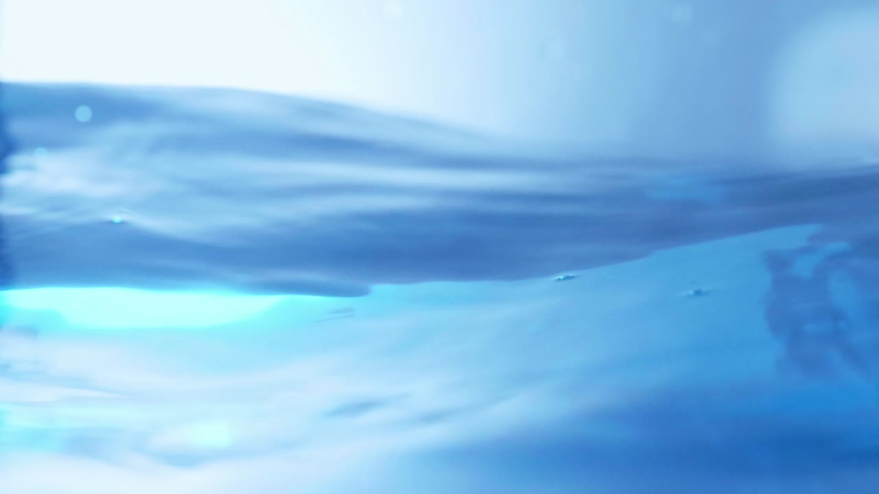 슬로우 모션의 깨끗한 물 표면은 물이 튀는 상점으로 화면을 채우고 기포로 액체 표면을 흔들고 있습니다.