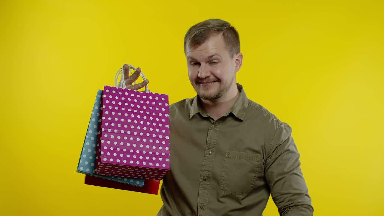 70%까지 할인된 인스크립션과 쇼핑 가방을 보여주는 남자, 낮은 가격에 만족하는 것처럼 보입니다.