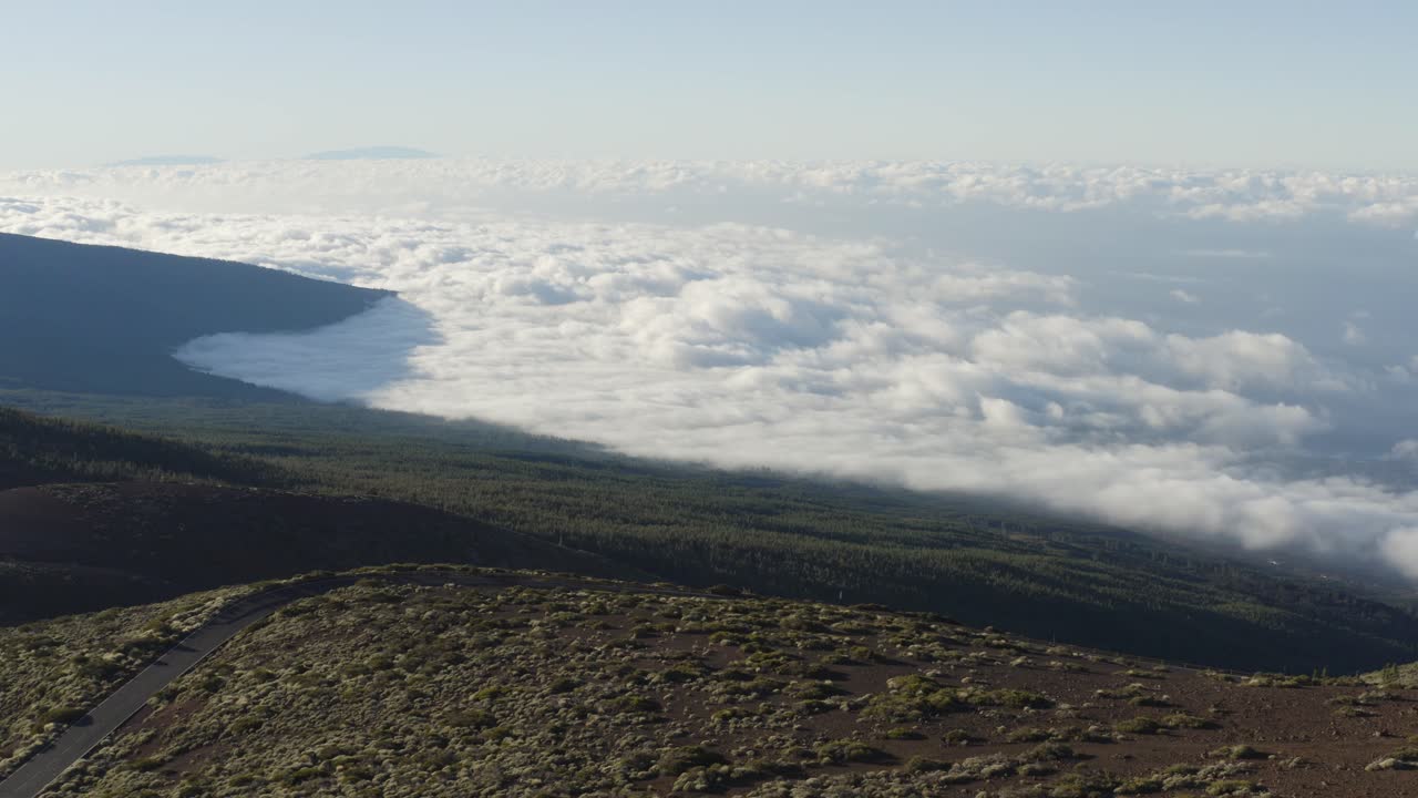 Lone car driving through the mountains and rolling clouds across Tenerife, Canary Islands.  Drone trailing left.