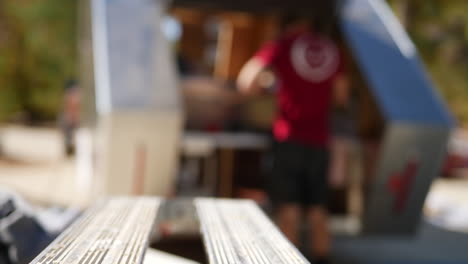 una mano agarrando un taladro inalámbrico con una broca mientras un trabajador de la construcción construye un remolque de viaje personalizado en un lugar de trabajo en el fondo con espacio para copiar