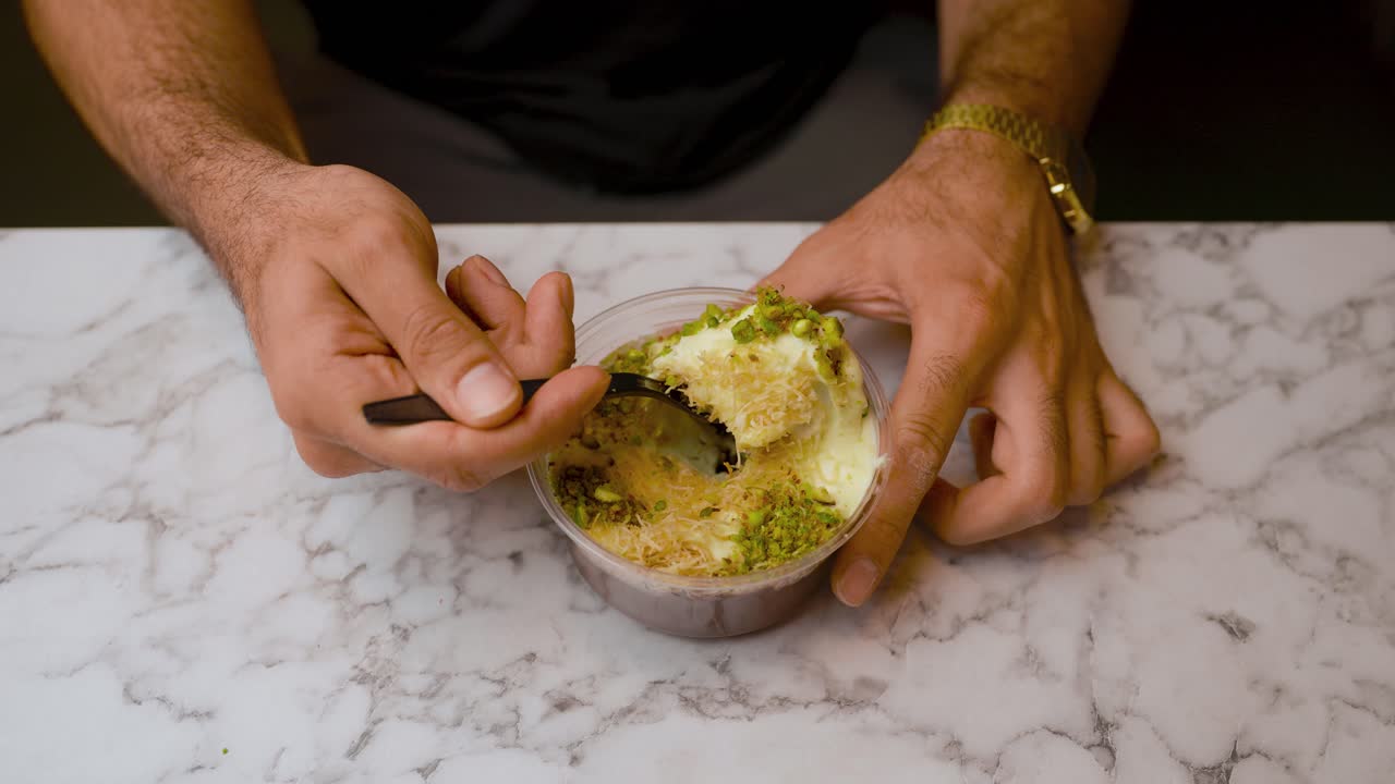 A man holds a spoon, lifting a portion of traditional Turkish dessert. Ideal for food, dessert, lifestyle, and cultural visuals