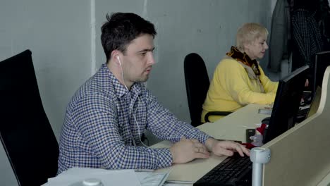 young guy with earphones work at computer in the office