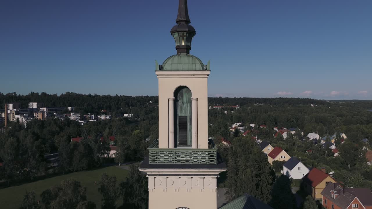 Kiehtova dronekuva Tampereen tuomiokirkosta Tampereella, Suomessa. Beigenvärinen kellotornikirkko kohoaa puiden latvojen ja kaupungin kattojen yläpuolelle, tarjoten upean näkymän kaupunkiin ja luontoon