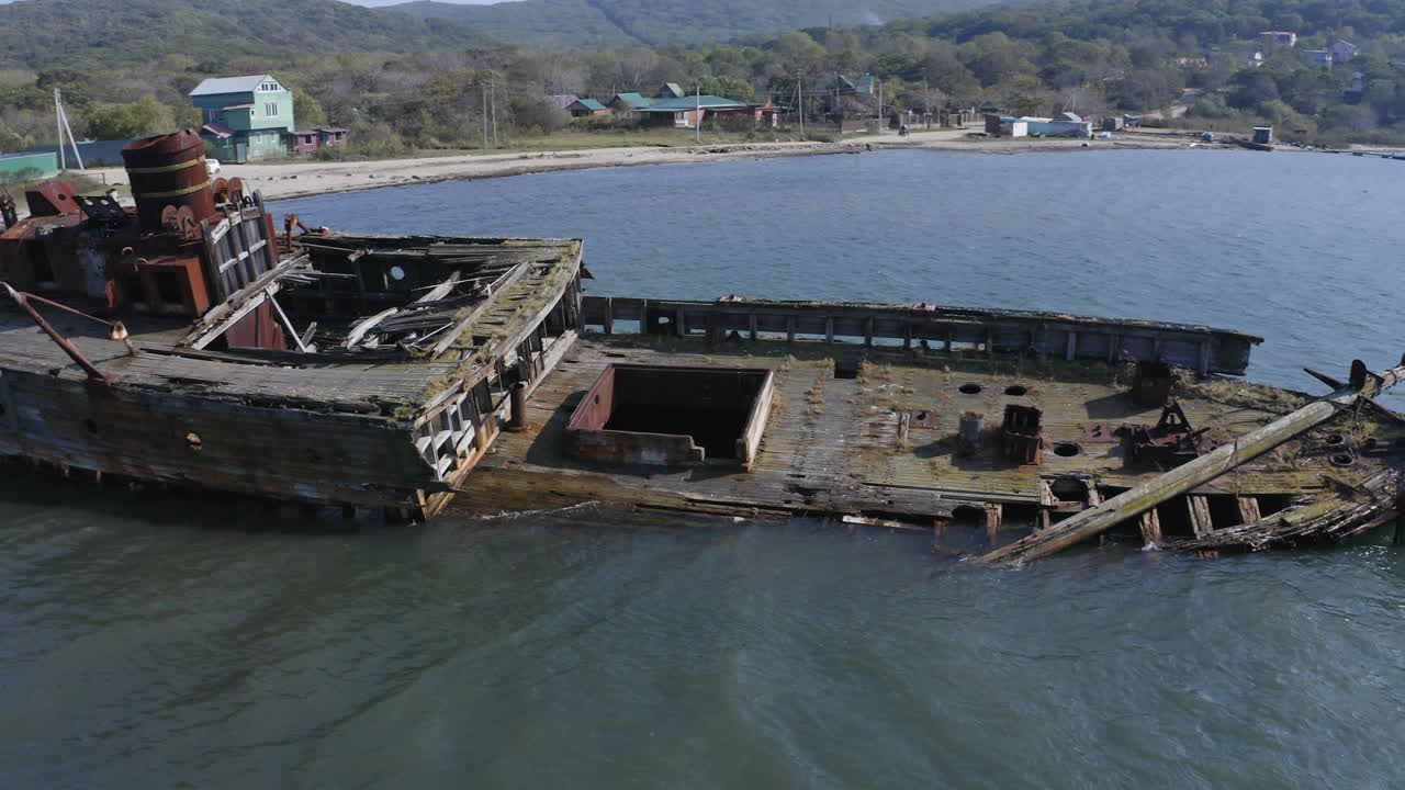Ships graveyard. Slow pass over the main deck of a derelict partially submerged shipwreck, inclined on its starboard side, aground near the shore.