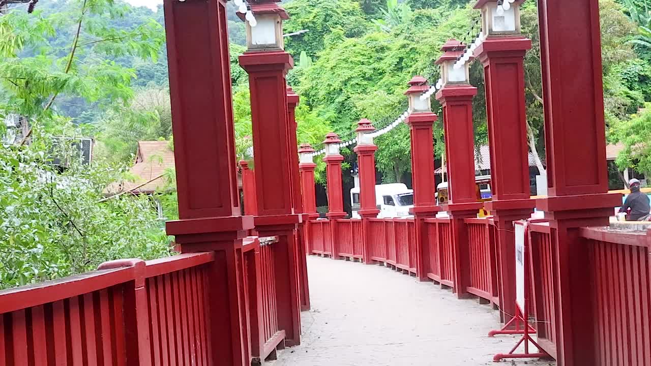 A striking red bridge with tall pillars set against a lush green landscape, showcasing architectural beauty.