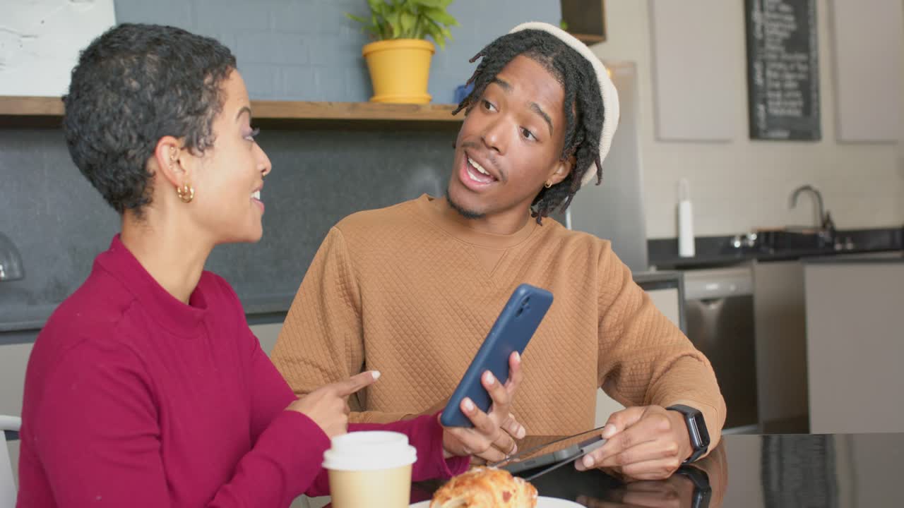 Diverse friends tapping smartphone and shifting tablet aside at cafe as man nodding absorbing info