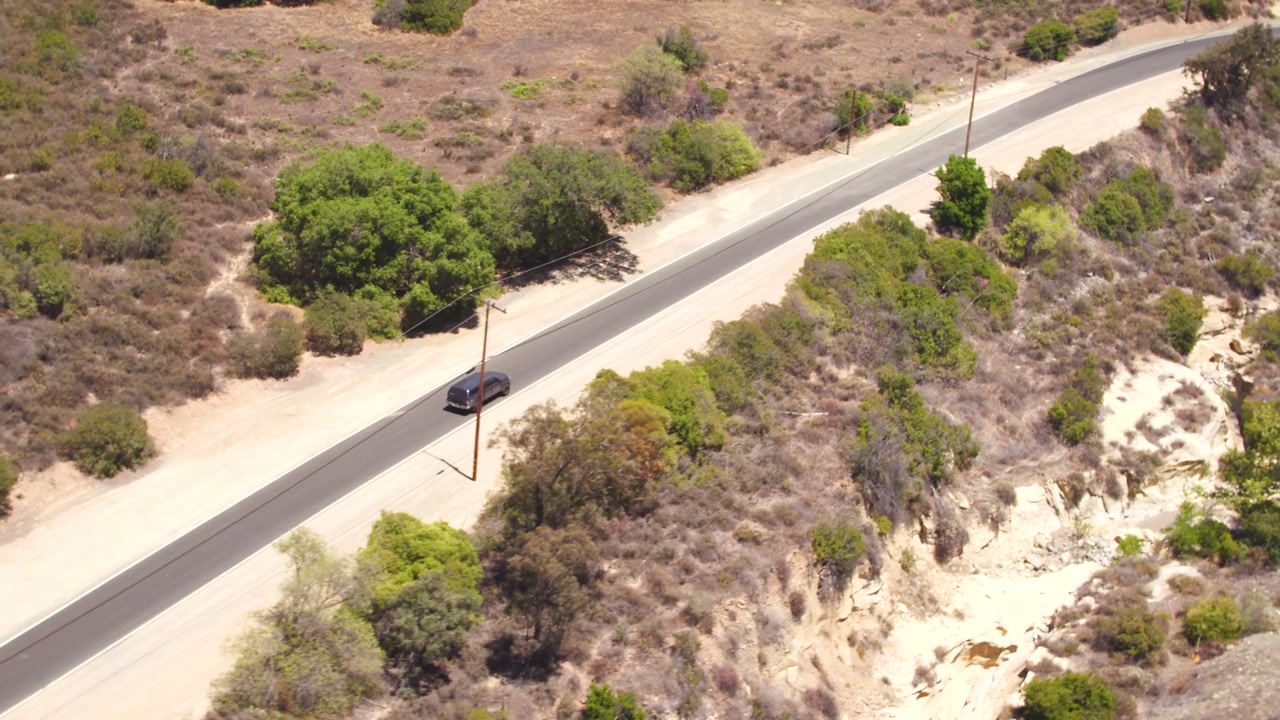 SUV aerial tracking driving down secluded single lane road.