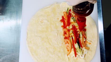 preparation of delicious snack. pouring red sauce on filling to cook pita. chef adds ketchup into meat and vegetable pita. top view