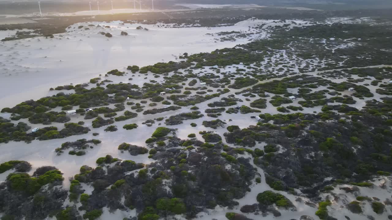 un avión no tripulado muestra un campamento junto a la playa con molinos de viento durante el amanecer