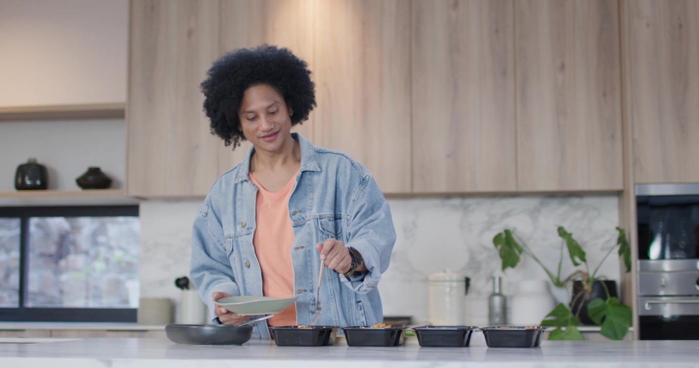 Donna afroamericana al bancone della cucina che nota dei vassoi, servendo su un piatto verde per la preparazione del pasto.