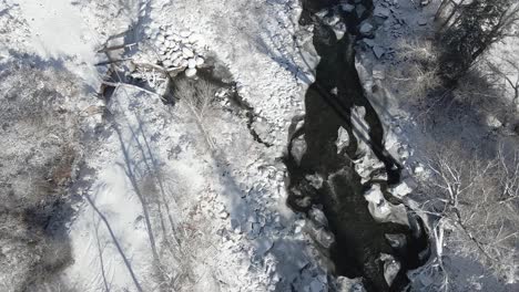 Imágenes-Aéreas-Que-Vuelan-A-Lo-Largo-Del-Río-águila-Con-Nieve-Fresca-En-El-Suelo-Y-Rocas-Y-árboles-Que-Bordean-La-Orilla