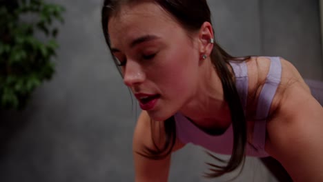 toma de primer plano de una chica atlética morena segura en una camiseta púrpura corriendo en el lugar usando una alfombra deportiva en un apartamento moderno en casa. chica morena segura siente sudor en su cara durante un ejercicio intenso en casa