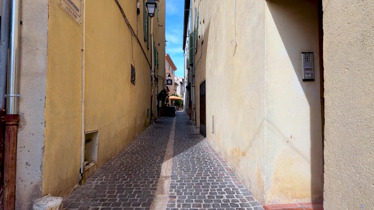 Kamerafahrt durch eine enge historische Gasse mit gelben Gebäuden unter hellem Sonnenlicht.