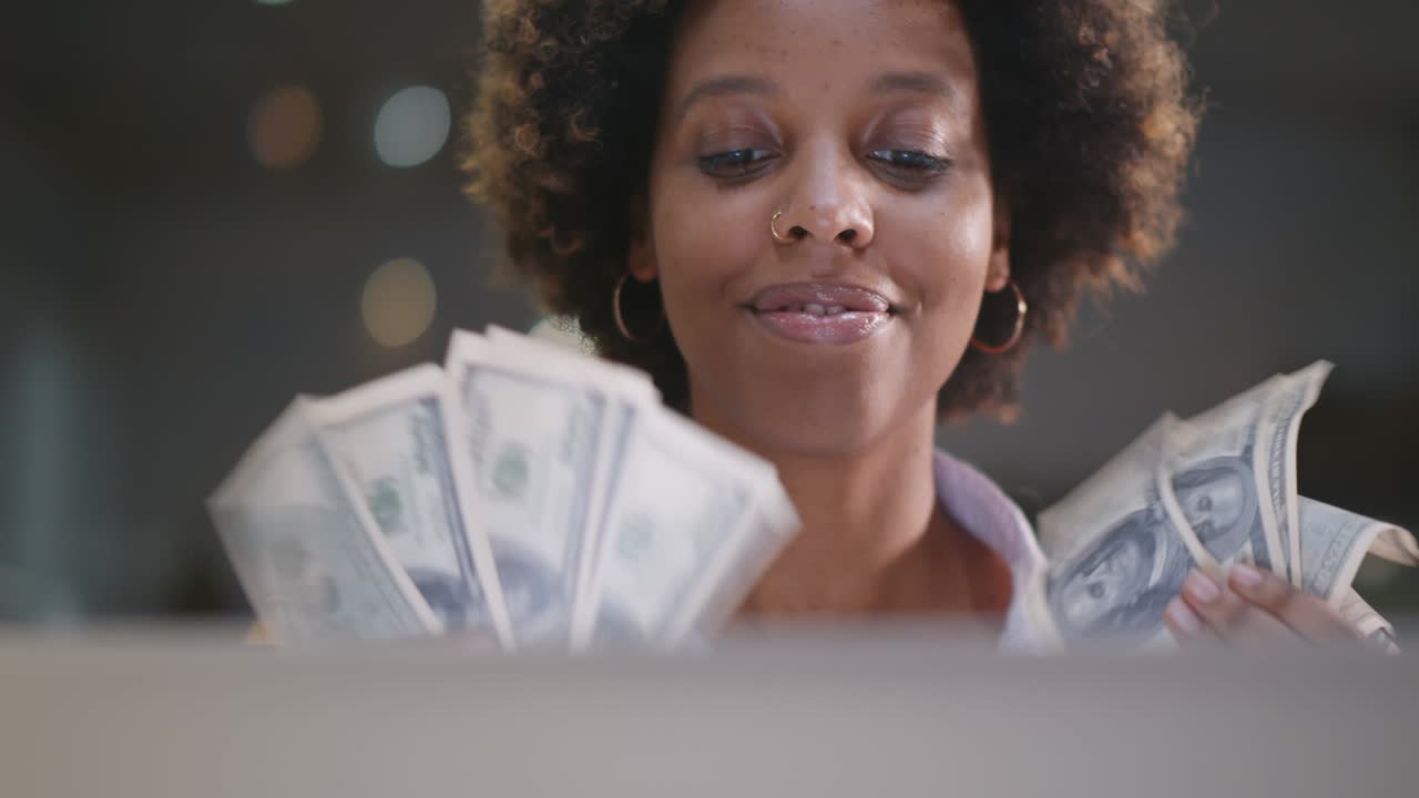 Happy african businesswoman sitting at workplace holding bunch of cash money