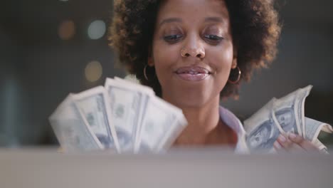 happy african businesswoman sitting at workplace holding bunch of cash money