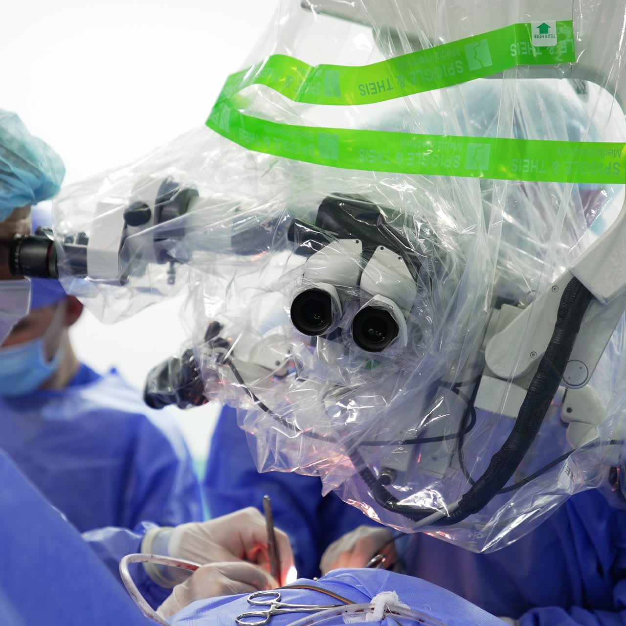 Group of medics use traditional surgical metal tools and advanced technological equipment in operation. Doctors look into microscope to perform surgery