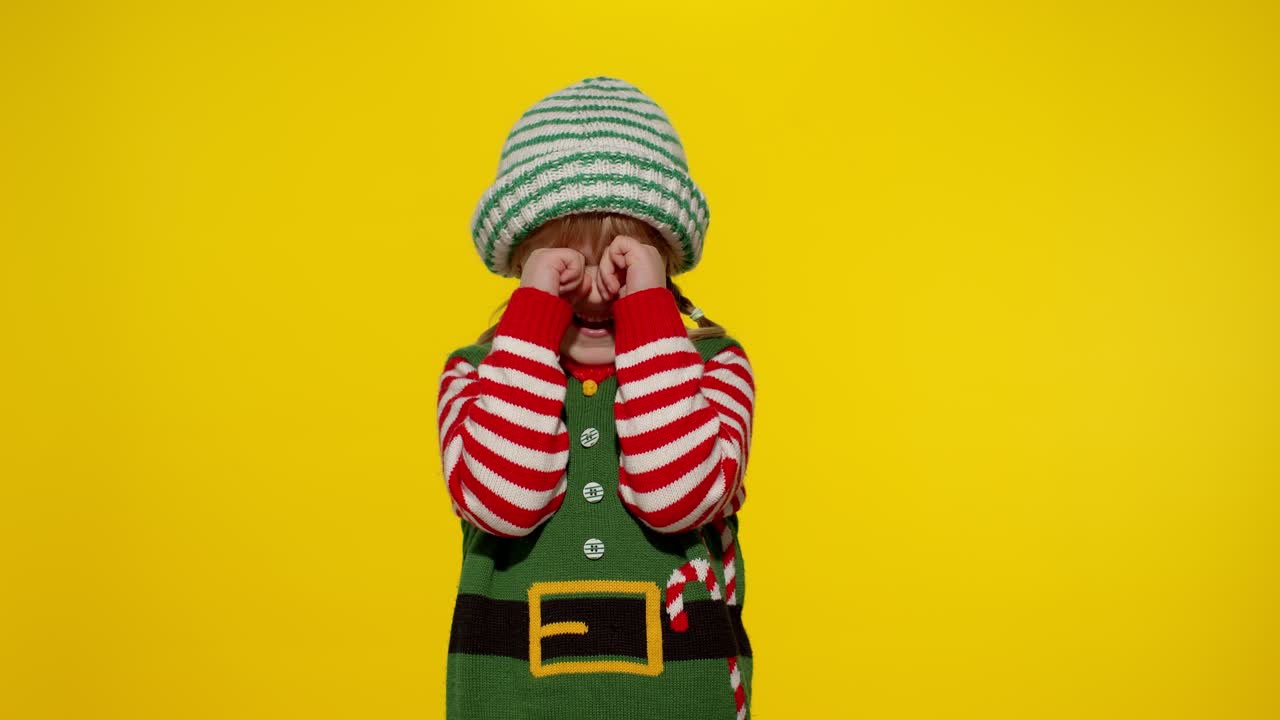 niña con disfraz de ayudante de santa claus llorando y limpiando las lágrimas. celebración de vacaciones de año nuevo