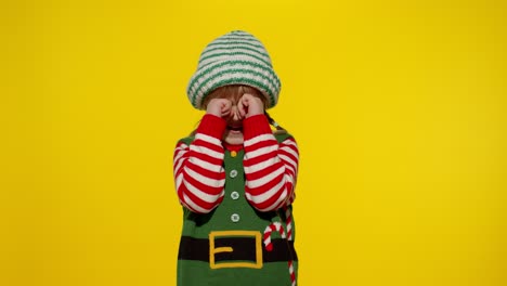 kid girl in christmas elf santa helper costume crying and wipes tears. new year holiday celebration