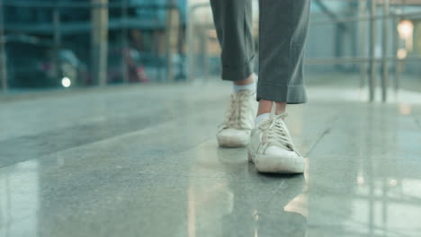 leg view of individual in white sneakers and gray trousers dancing on polished tile floor with glass building and iron railing in background