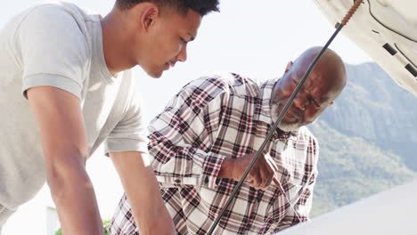 african american father showing adult son how to check oil in car, slow motion