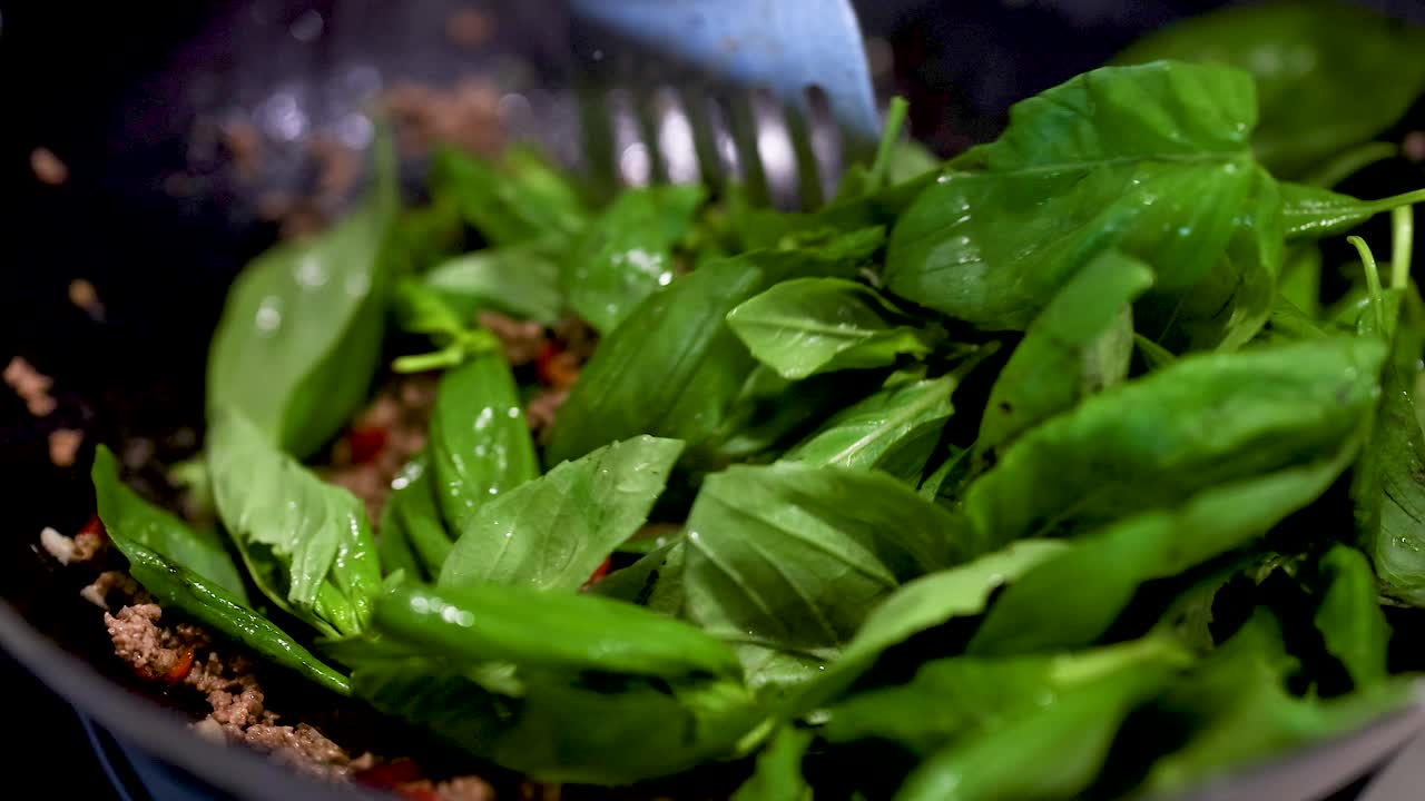 Close-up of beef and basil stir-fry preparation in a kitchen setting with vibrant greens and rich textures
