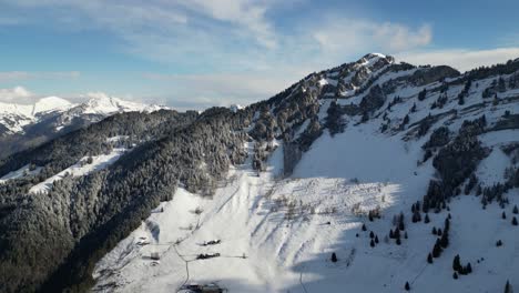 Dense-snow-coveres-mountain-slopes-and-banded-ridges-with-pine-tree-forest-on-blue-sky-day