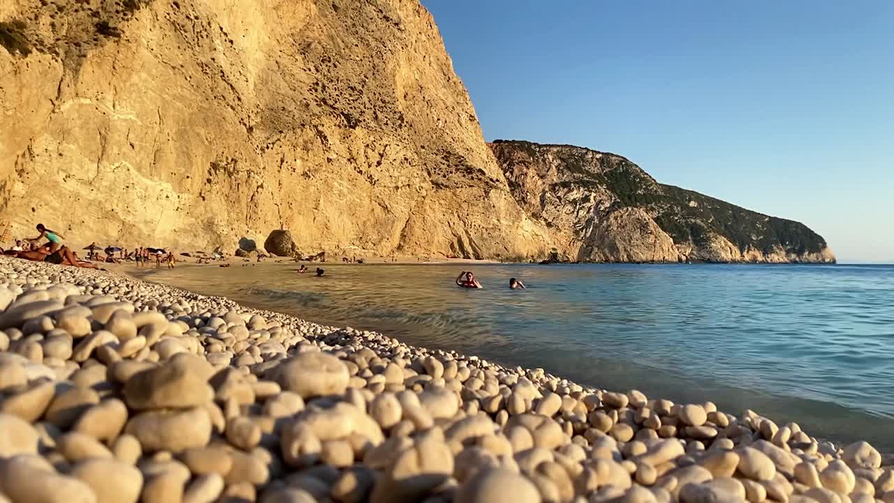 Tranquil island seaside with rocky shore, waves gently lapping, peaceful and scenic view from low angle of pebble beach as people play in water