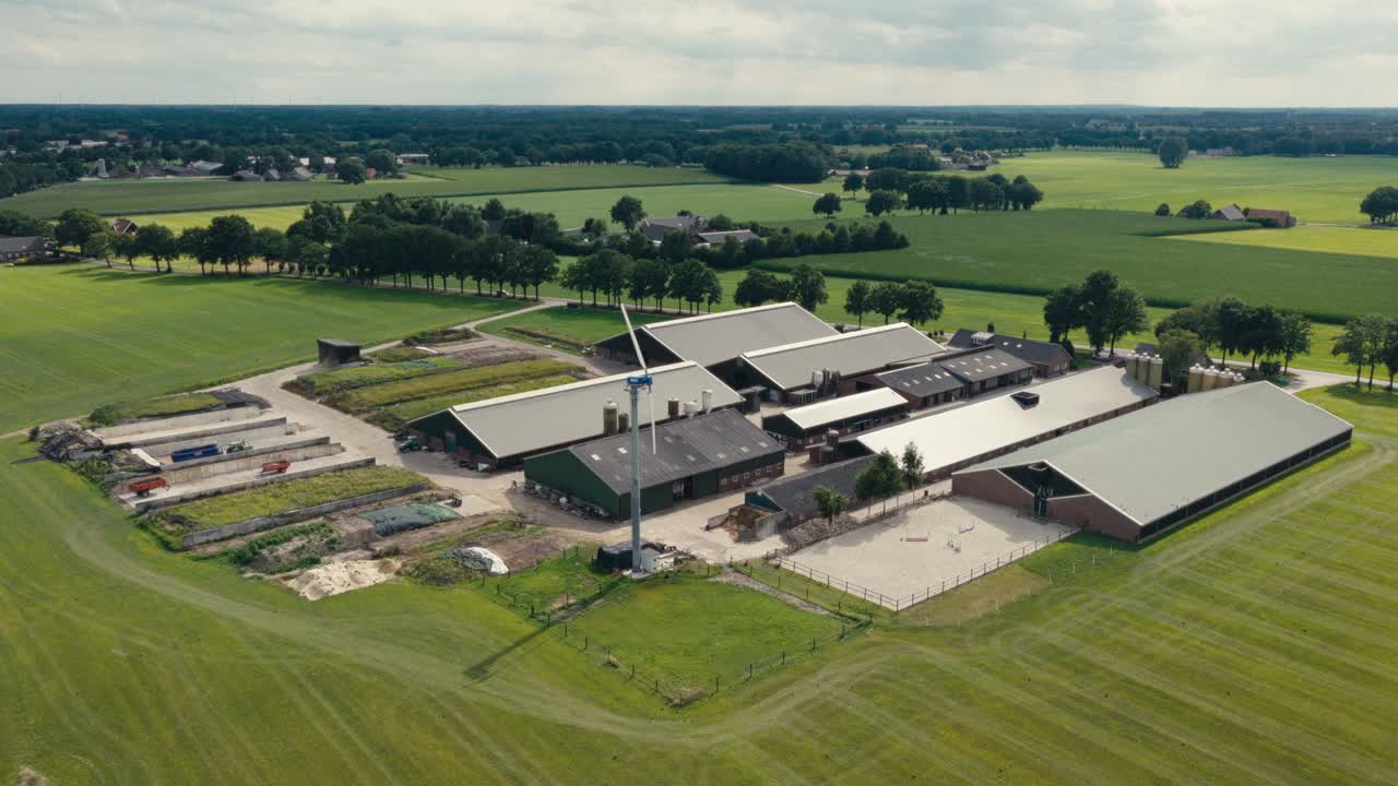 Drone shot of a large farm complex with green rooftops and surrounding fields under a clear sky in the countryside