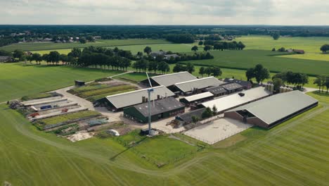 drone shot of a large farm complex with green rooftops and surrounding fields under a clear sky in the countryside