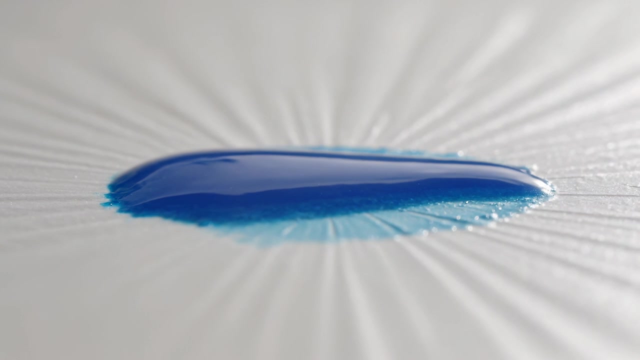 Schwerkraft zieht zähflüssigen blauen Tropfen, der sich auf einer makro-radialen Tischplattenoberfläche ausbreitet, mit Glanzlichtern
